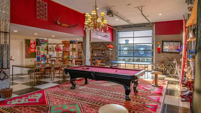 The Farmhouse game room with a red felt pool table, brass chandelier, Persian rug, and vintage bar seating