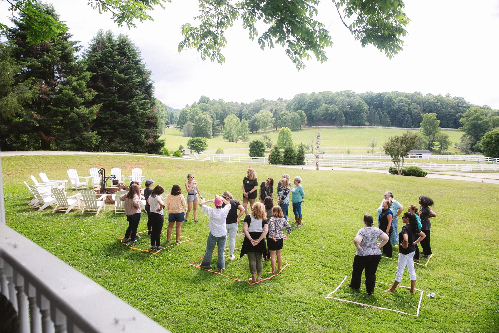 A group gathered in a wide circle of chairs on the lawn at The Horse Shoe Farm with white fences behind them