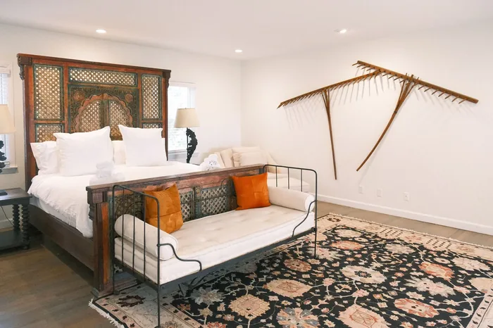 A guest suite at The Horse Shoe Farm with a white iron daybed, orange throw pillows, patterned area rug, and rustic wall art