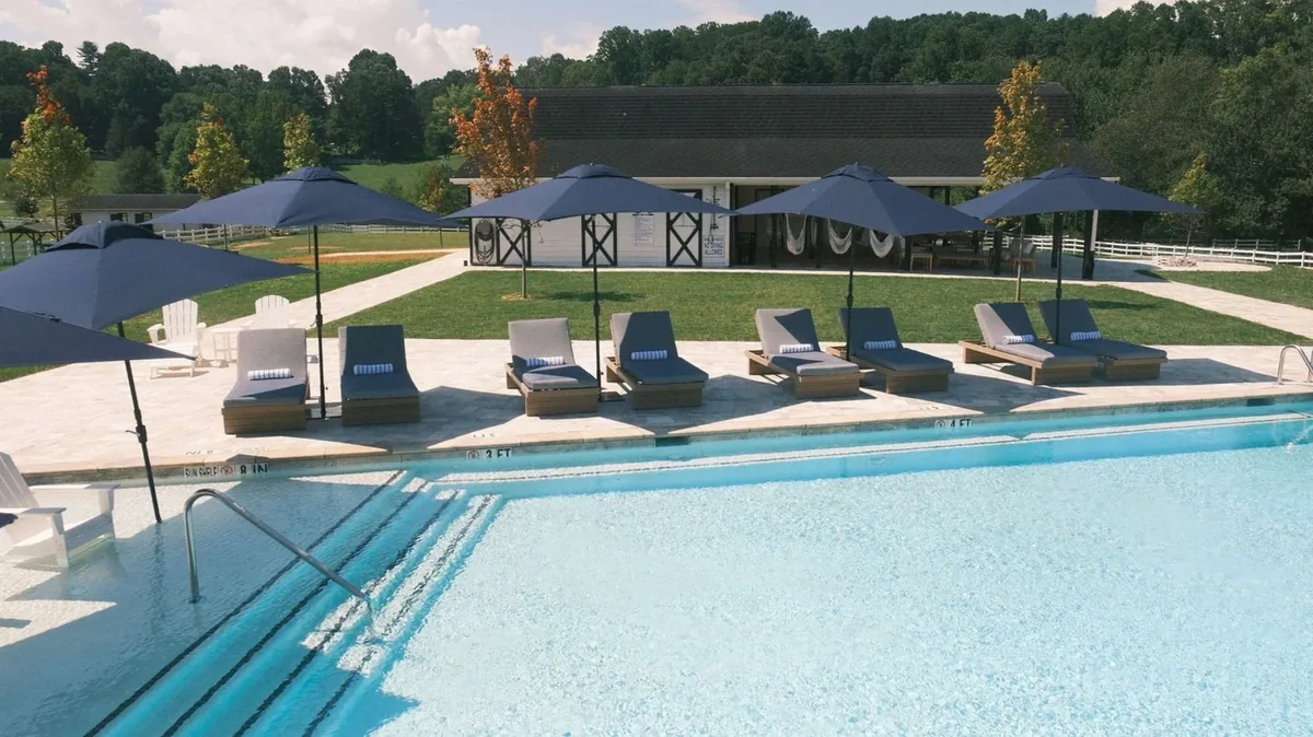 Poolside patio at The Horse Shoe Farm with navy umbrellas, teak loungers, and the white pool house overlooking Blue Ridge Mountain views